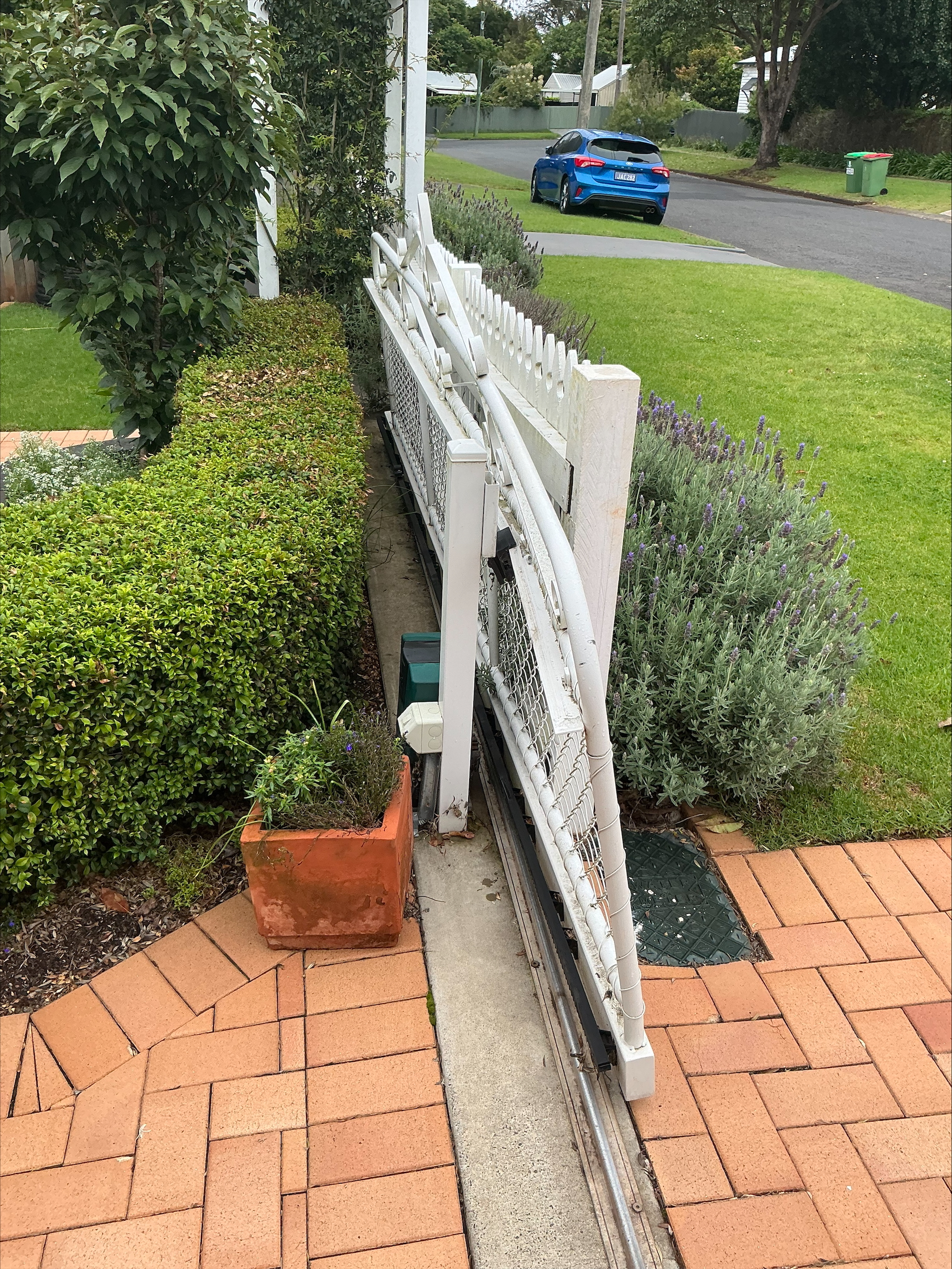 Leaning and twisted white sliding gate with rusted frame before repair